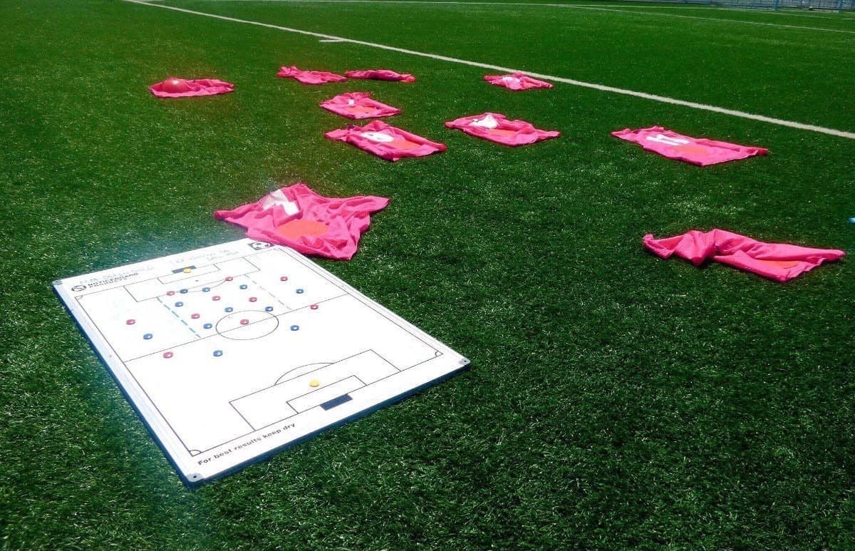 A coach's tactical board and training bibs laid out on a sports pitch