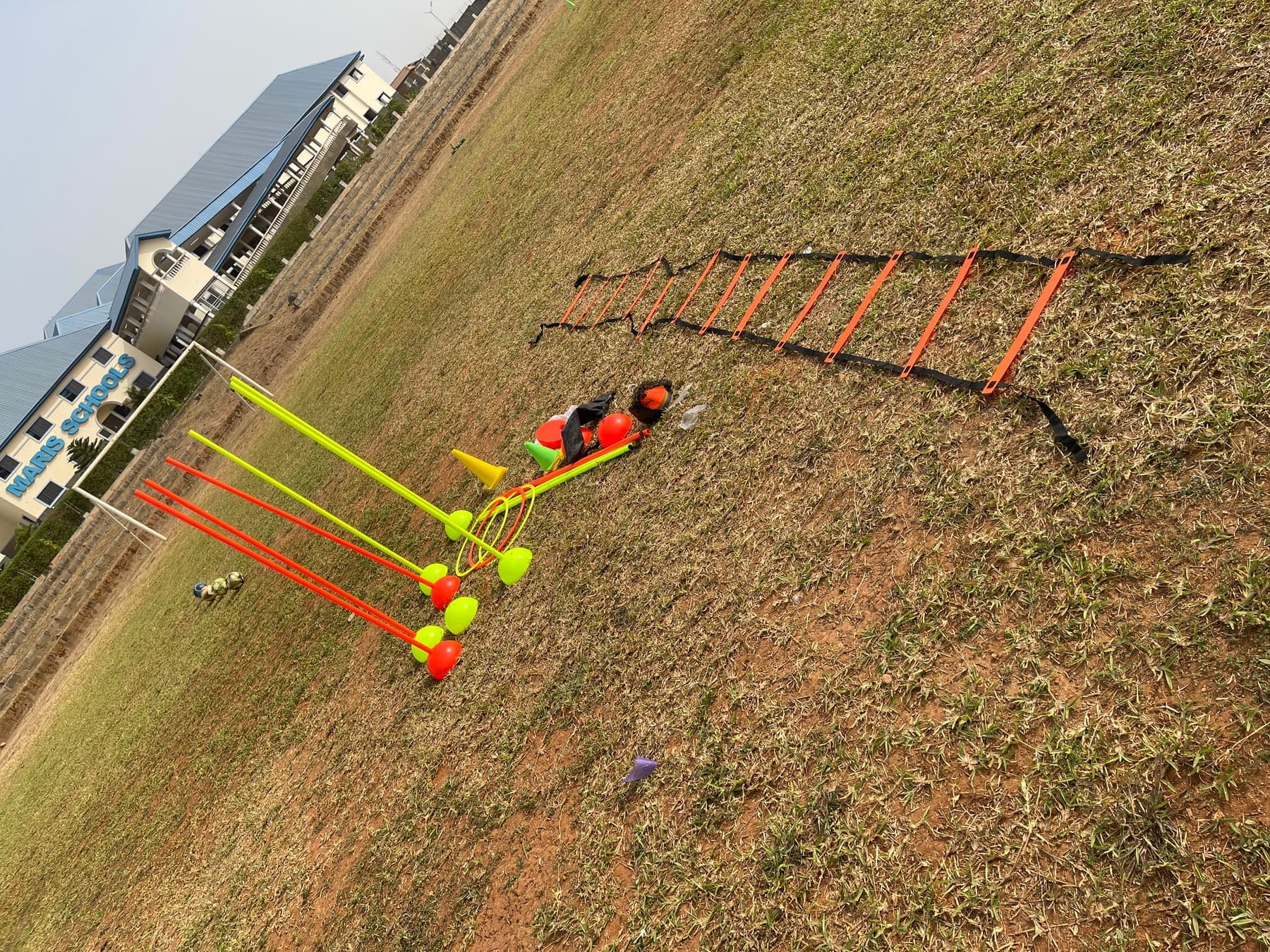 An agility ladder, coloured poles and cones laid out on a dry training field