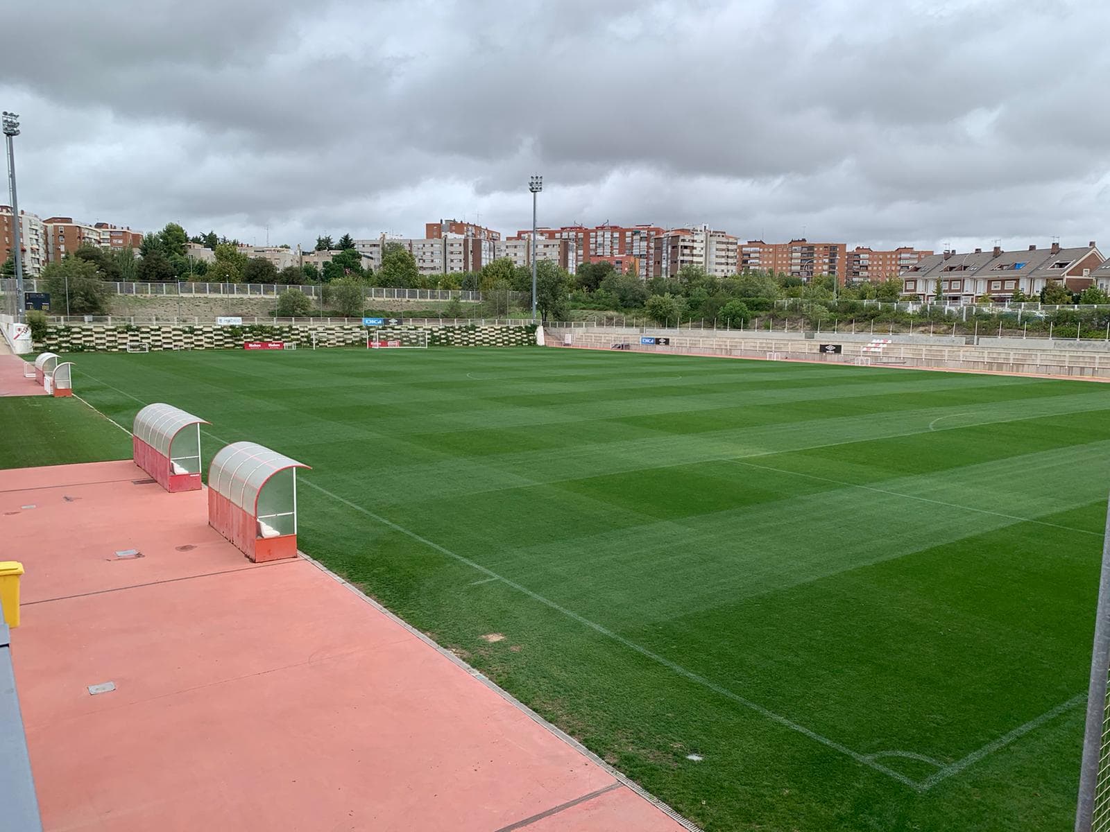 A grass sports pitch with dugouts under an overcast sky