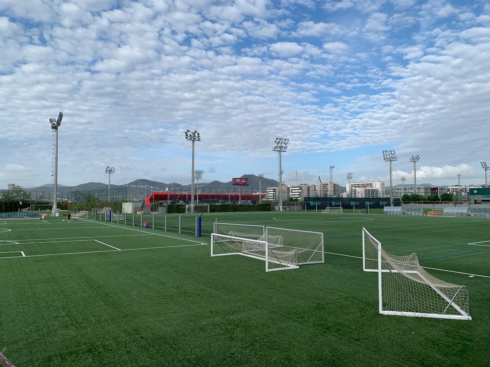 An artificial-turf training complex with floodlights and small goals under a cloudy sky