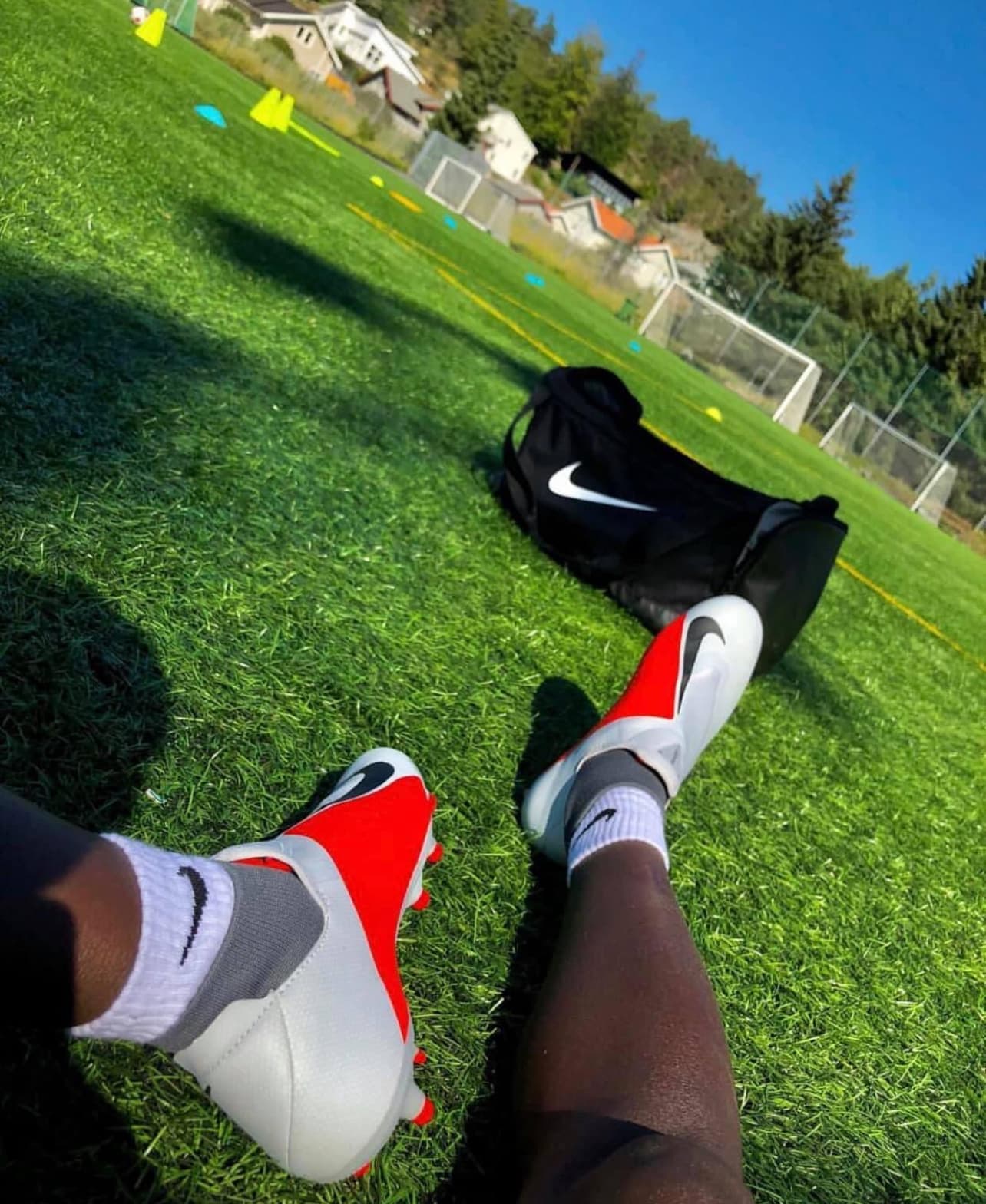 A player's boots and kit bag on bright green turf beside training cones